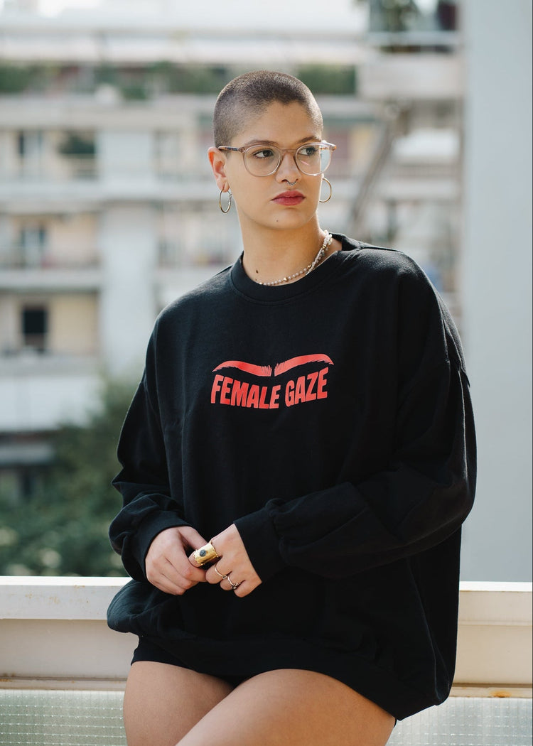 Person wearing a black sweatshirt with 'FEMALE GAZE' text, standing outdoors.