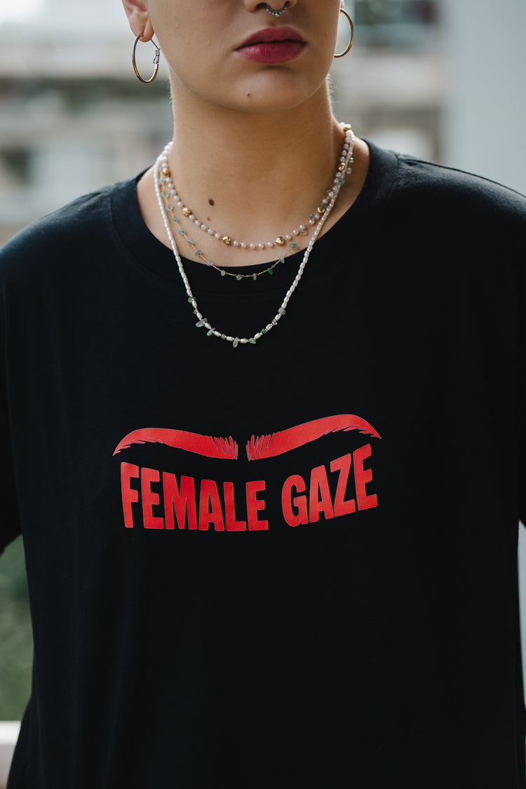 Person wearing a black t-shirt with 'FEMALE GAZE' in red text.