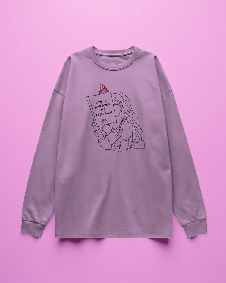 pink long sleeve t-shirt with graphic design of a person holding a book titled 'How to Burn Down the Patriarchy' on a purple background.