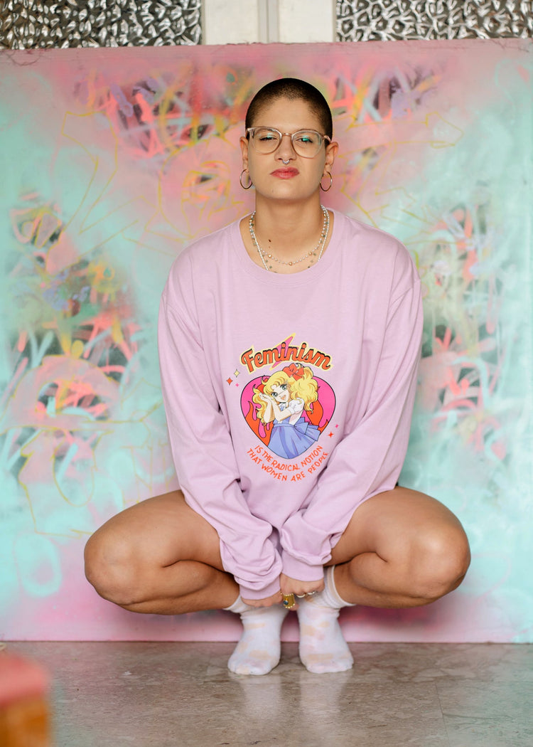 Person wearing a pink sweatshirt with a graphic design, sitting in front of a colorful floral wall.