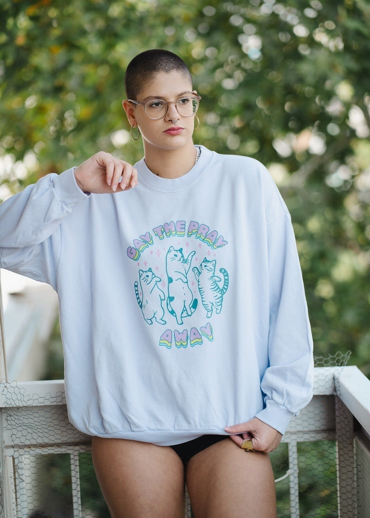 Person wearing a light blue sweatshirt with cat graphics and text, standing outdoors.