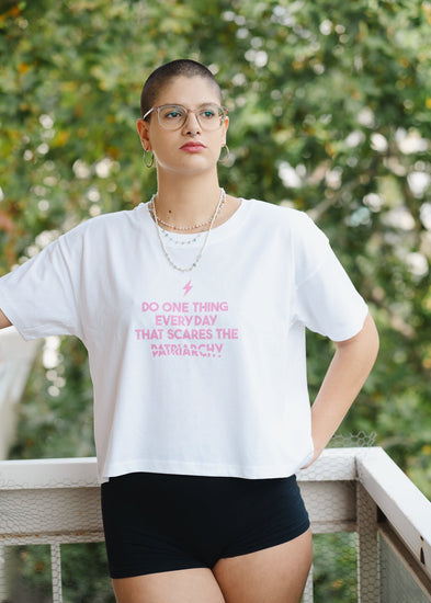 Person wearing a white t-shirt with pink text, standing outdoors with greenery in the background