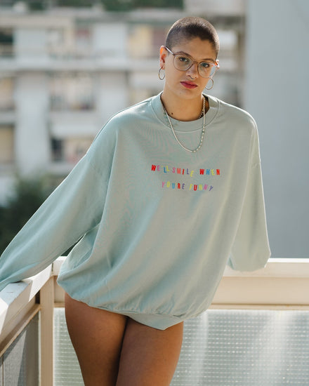 Person wearing a light blue sweatshirt with colorful text on a balcony