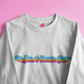 White sweatshirt with colorful text design on a pink background
