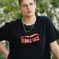 Person wearing a black t-shirt with 'FEMALE GAZE' text, standing outdoors.