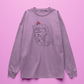 pink long sleeve t-shirt with graphic design of a person holding a book titled 'How to Burn Down the Patriarchy' on a purple background.