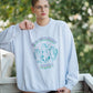 Person wearing a light blue sweatshirt with cat graphics and text, standing outdoors.