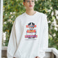 Person wearing a white sweatshirt with a graphic design outdoors