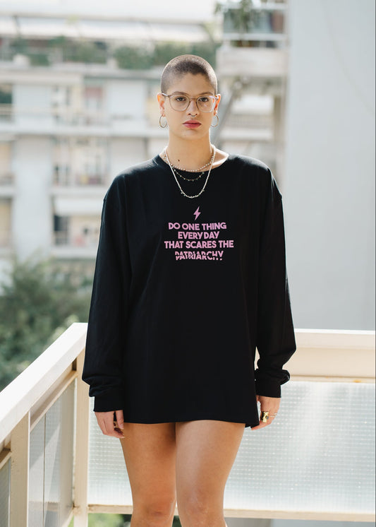 Person wearing a black sweatshirt with text on it, standing on a balcony.