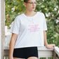 Person wearing a white t-shirt with text and black shorts on a balcony