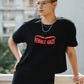 Person wearing a black t-shirt with 'FEMALE GAZE' text, standing outdoors.