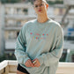 Person wearing a light blue sweatshirt with colorful text, standing on a rooftop.